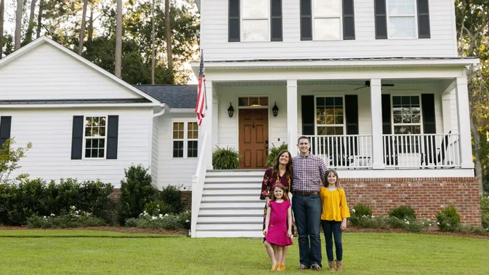 A young family posing in front of their Victorian house.