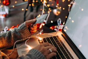 woman hand holding credit card in front of a laptop with fairy lights