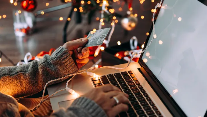 woman hand holding credit card in front of a laptop with fairy lights