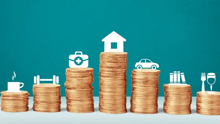 pila de monedas con iconos arriba de café, ejercicio, botiquín de primeros auxilios, casa, auto, libros, comida