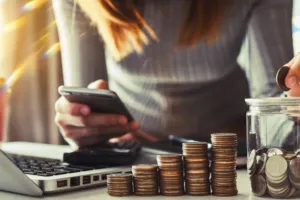 A person standing over a laptop while counting a coin jar