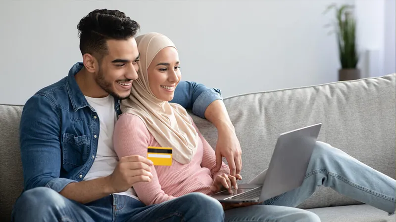 Young couple staring at a computer screen, smiling with a credit card in hand.