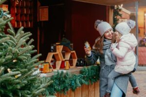 Mujer de compras navideñas con un niño frente al escaparate de una tienda con un árbol de Navidad