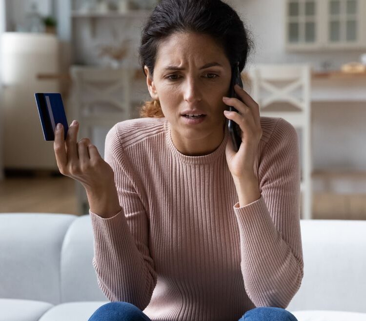 A frustrated person talking on the phone and holding up their credit card