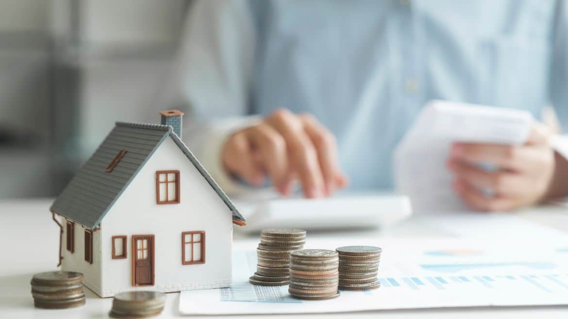 small plastic house with dark roof and red trimmed windows and stacks of coins next to the house.