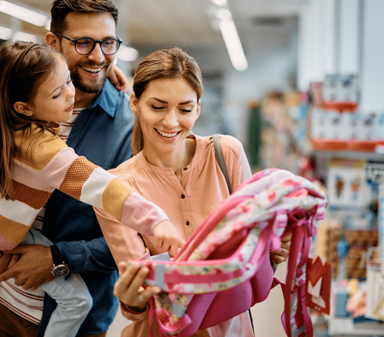Little girl and her parents choosing backpack for school while shopping in store together.
